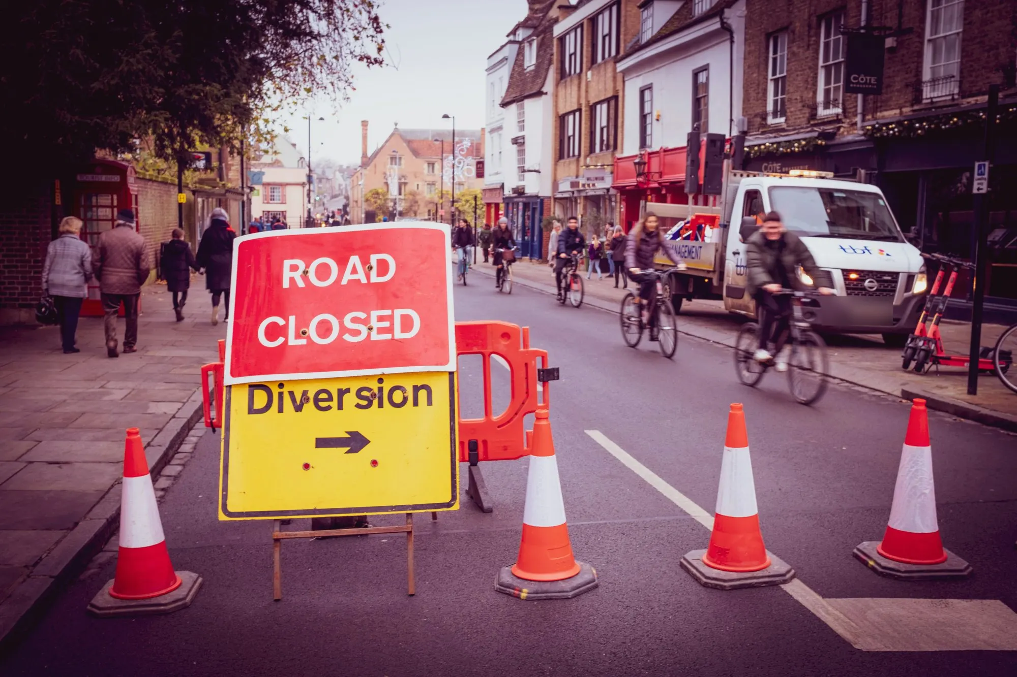 Road closed and diversion signs with cones across a town-centre street